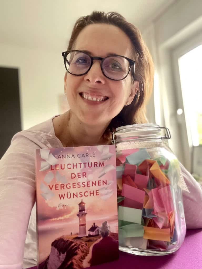 Lächelnde Anna Carle mit ihrem Buch und Wünscheglas.