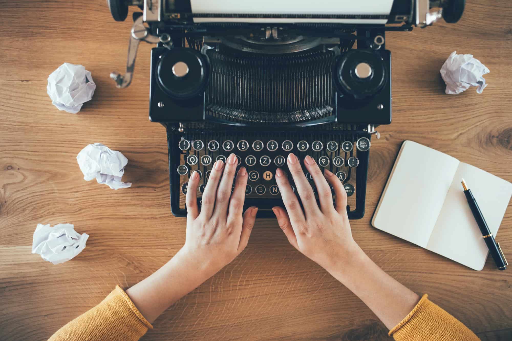 Frau tippt an Buchmanuskript auf Schreibmaschine – kreativer Schreibprozess